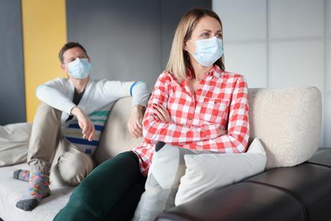 A woman wearing a mask turns away from her husband with her arms crossed